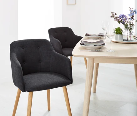 Deux chaises rembourrées anthracite avec accoudoirs et une table en bois avec des fleurs et des assiettes dans une salle à manger.