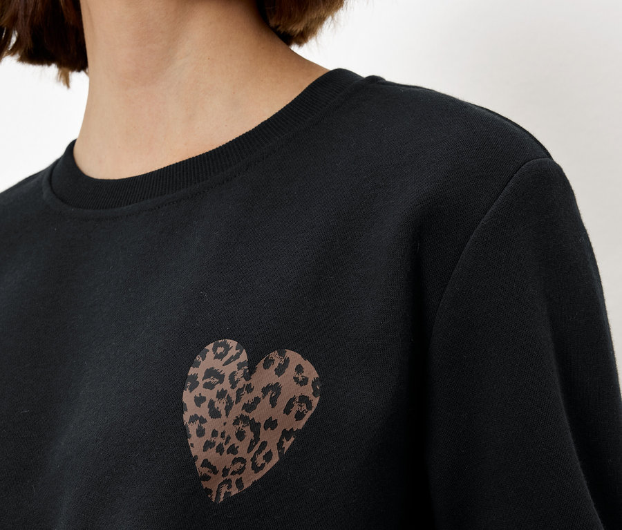 Une femme porte un sweat-shirt noir avec un cœur léopard.