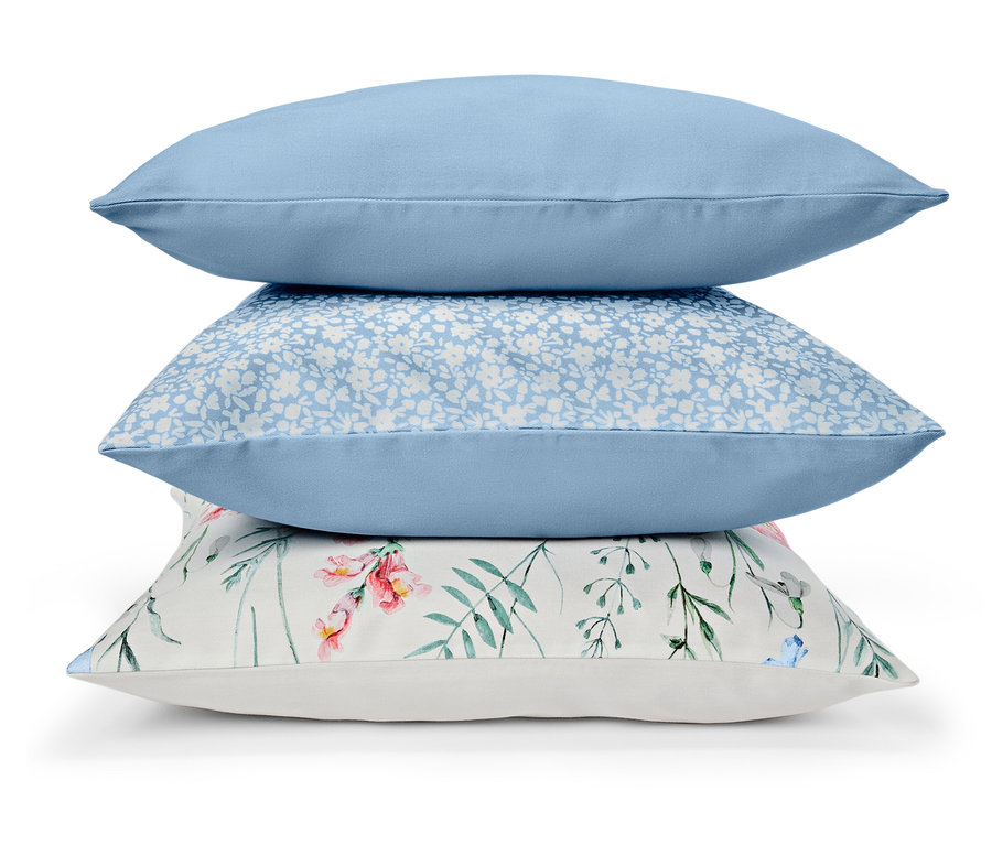 Trois coussins sont empilés : bleu uni, bleu à fleurs blanches et blanc à motifs floraux.