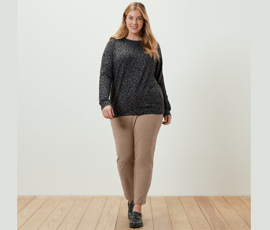 Femme marchant et portant un t-shirt chauve-souris imprimé et un pantalon de jogging beige.