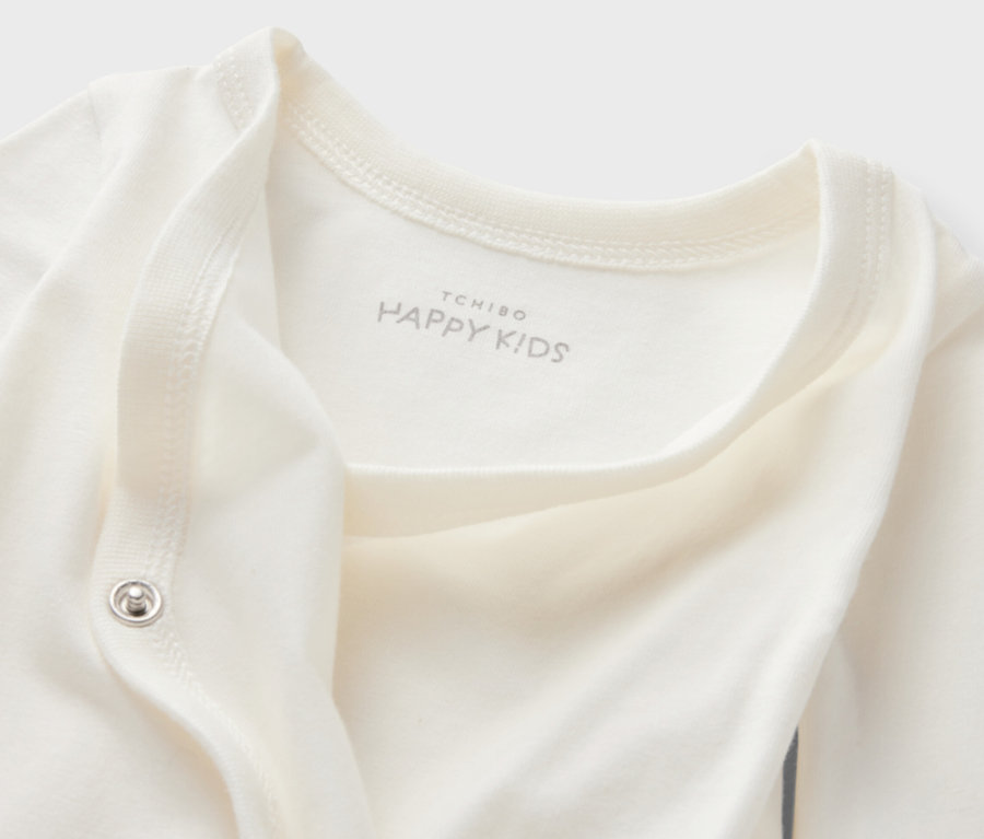 Gros plan sur un body blanc évolutif pour bébé (lot de 5) avec le logo Tchibo Happy Kids.