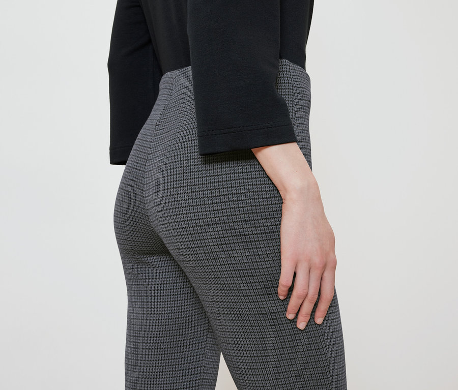 Gros plan d'une femme portant un pantalon à motifs et un chemisier noir.