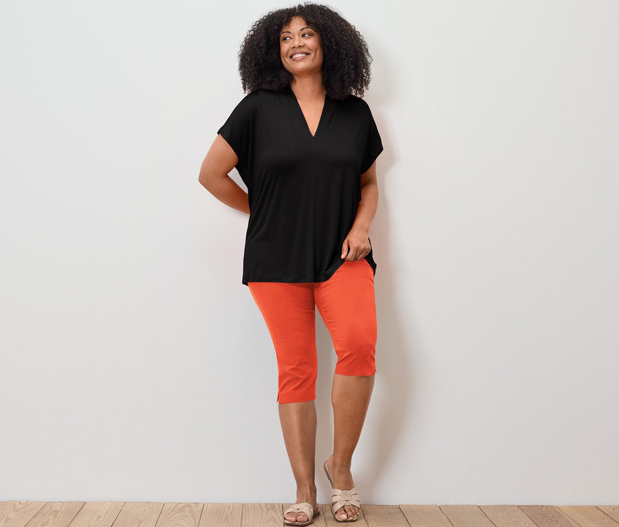 Femme posant en blouse avec encolure en V, noir et pantalon 3/4 stretch, orange.