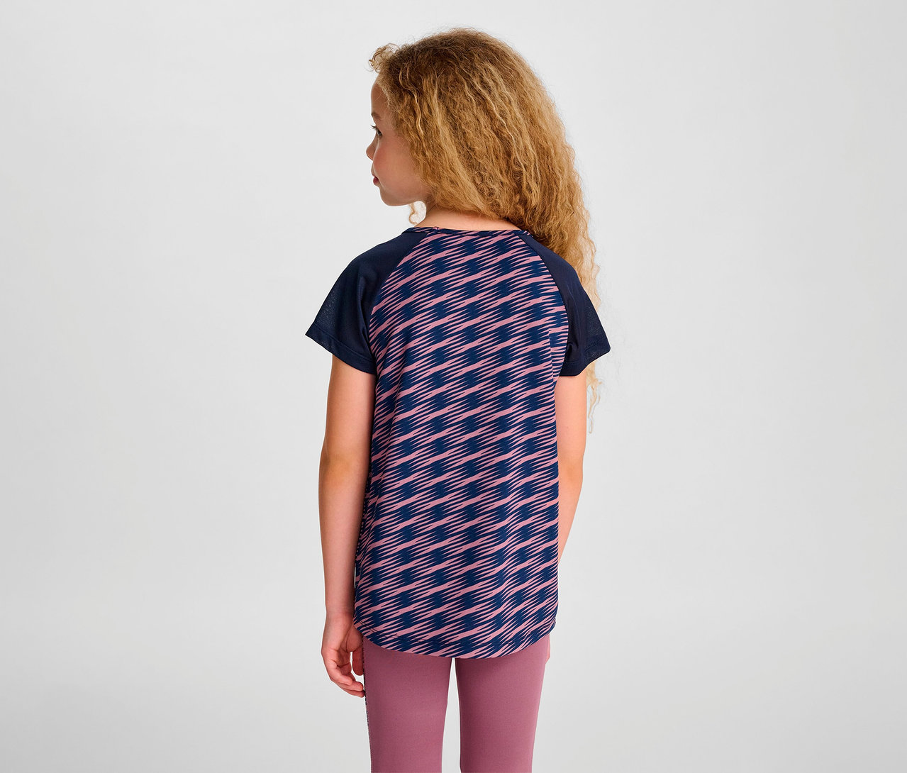 Une fille, vue de dos, porte un t-shirt S/S HUMMEL HMLJR Mix et un legging rose.