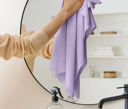 Femme nettoyant un miroir avec un chiffon violet.
