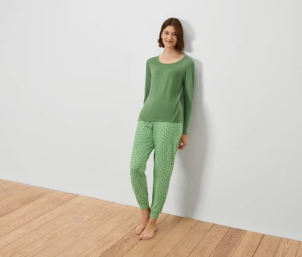 Une femme en pyjama vert est adossée à un mur blanc.