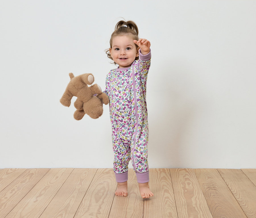 Un enfant en combinaison fleurie se tient avec un ours en peluche.