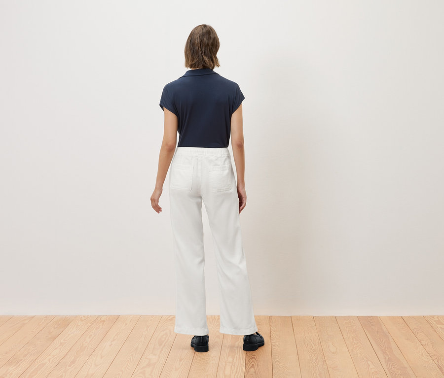 Une femme se tient dos tourné, portant un polo bleu marine et un pantalon blanc.