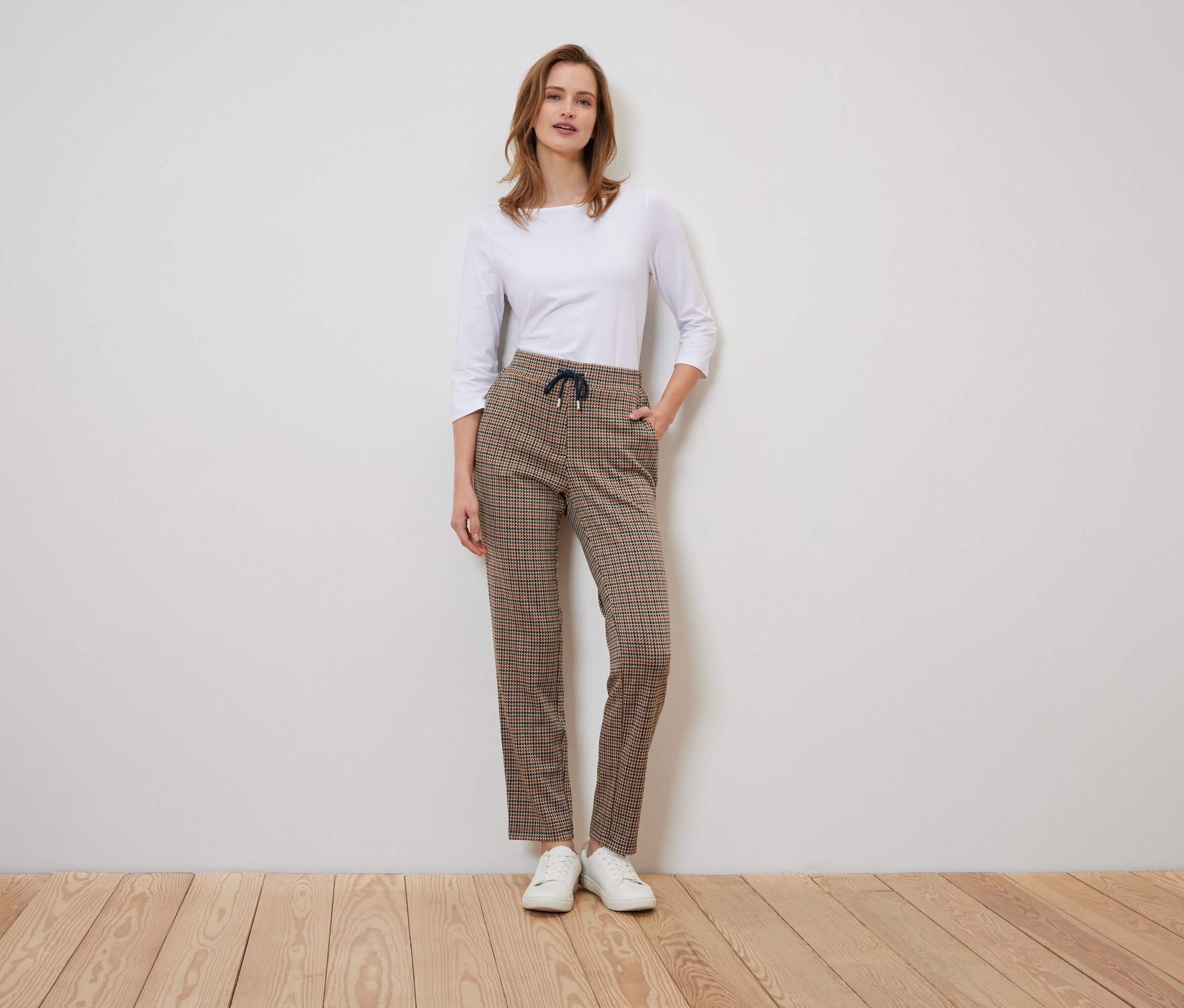 Une femme se tient debout et pose dans un pantalon à carreaux et une chemise blanche.
