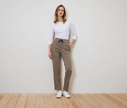 Une femme se tient debout et pose dans un pantalon à carreaux et une chemise blanche.