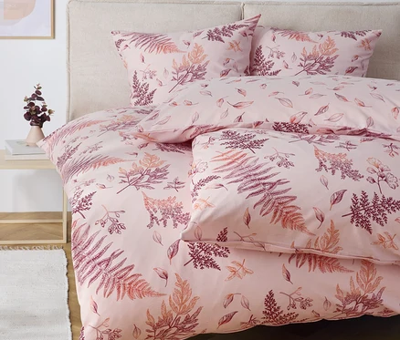 Linge de lit rose avec motif de fougères sur un lit.