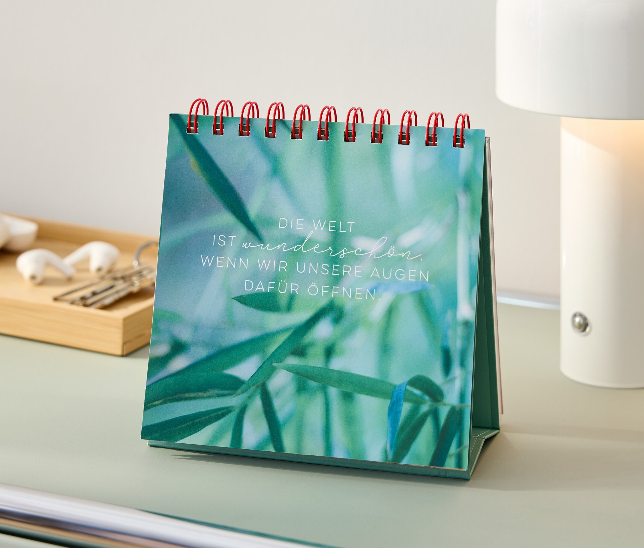 Sur une table se trouve un livre à poser « Sommerträume » (en allemand) avec une spirale rouge, à côté d'une lampe, d'écouteurs et de clés.