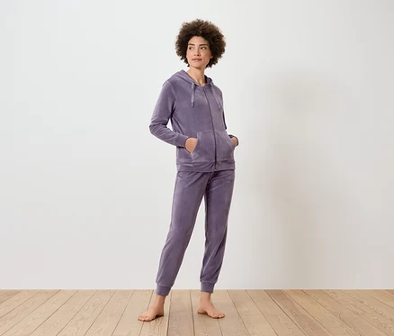 Une femme debout porte un survêtement violet avec un sweat à capuche et un pantalon de jogging.