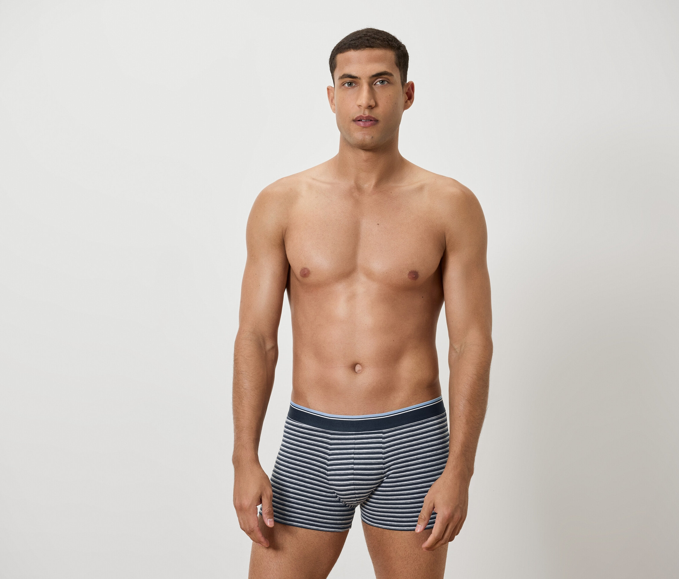 Un homme torse nu pose en caleçon rayé bleu et blanc.