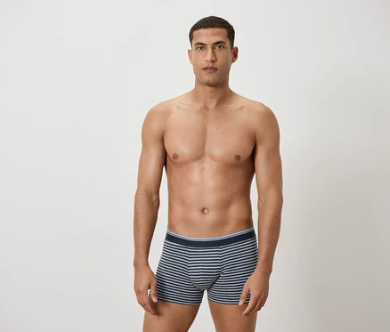 Un homme torse nu pose en caleçon rayé bleu et blanc.