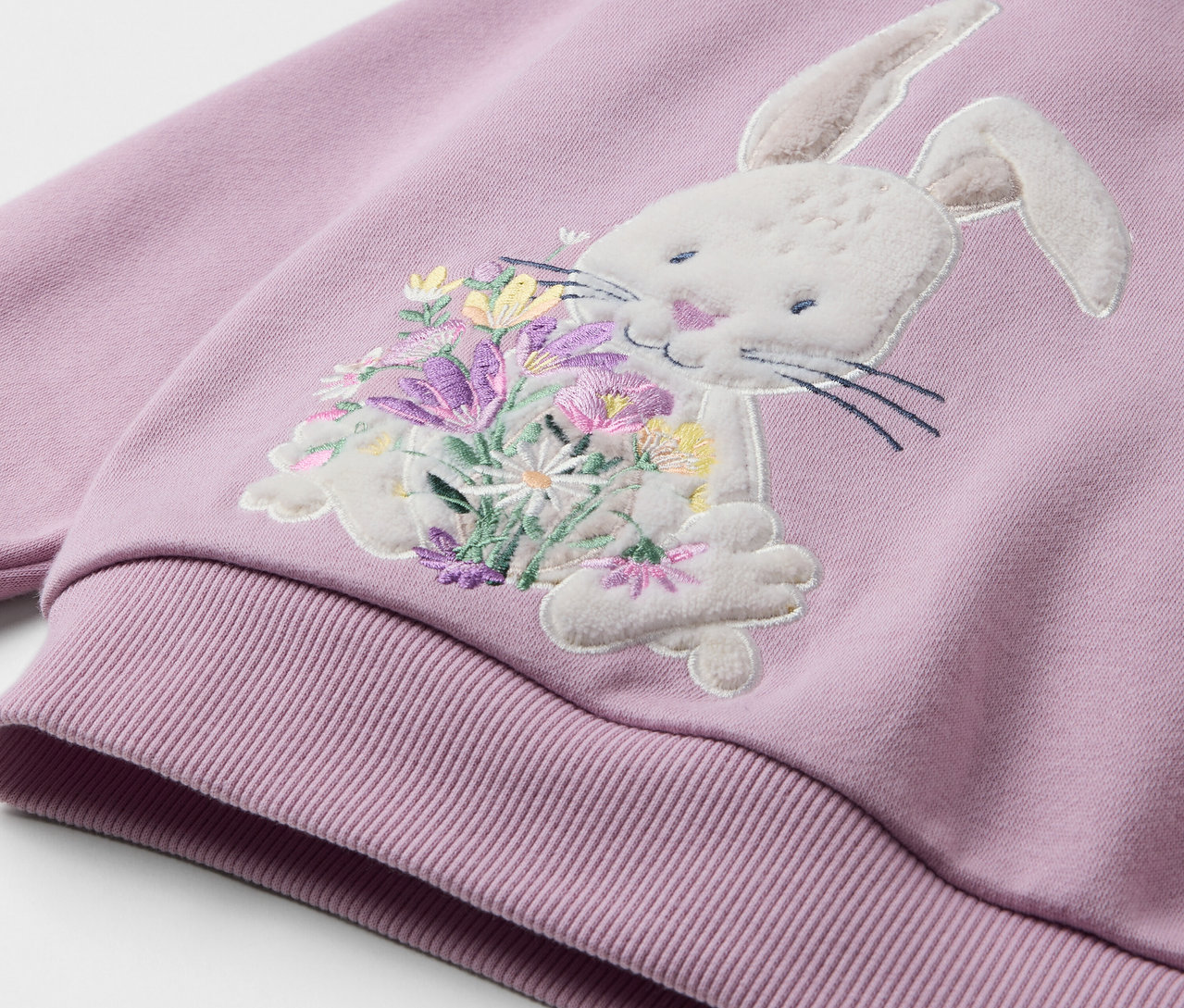 Gros plan sur un sweat-shirt lilas clair avec un appliqué de lapin tenant un bouquet de fleurs.