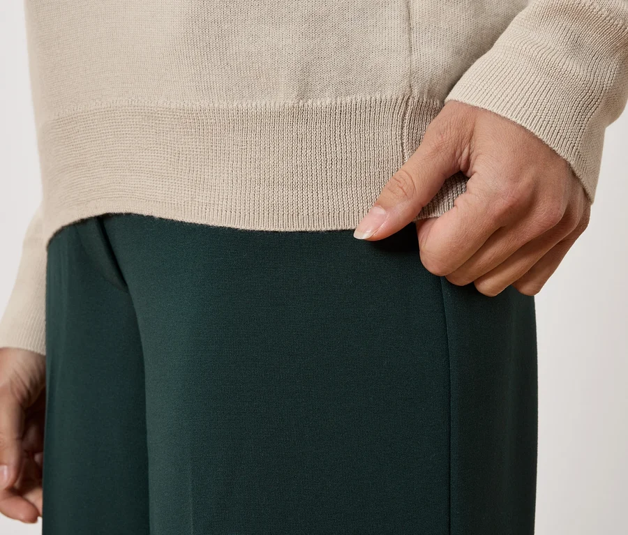 Gros plan d'une personne portant un pull beige et un pantalon vert foncé.