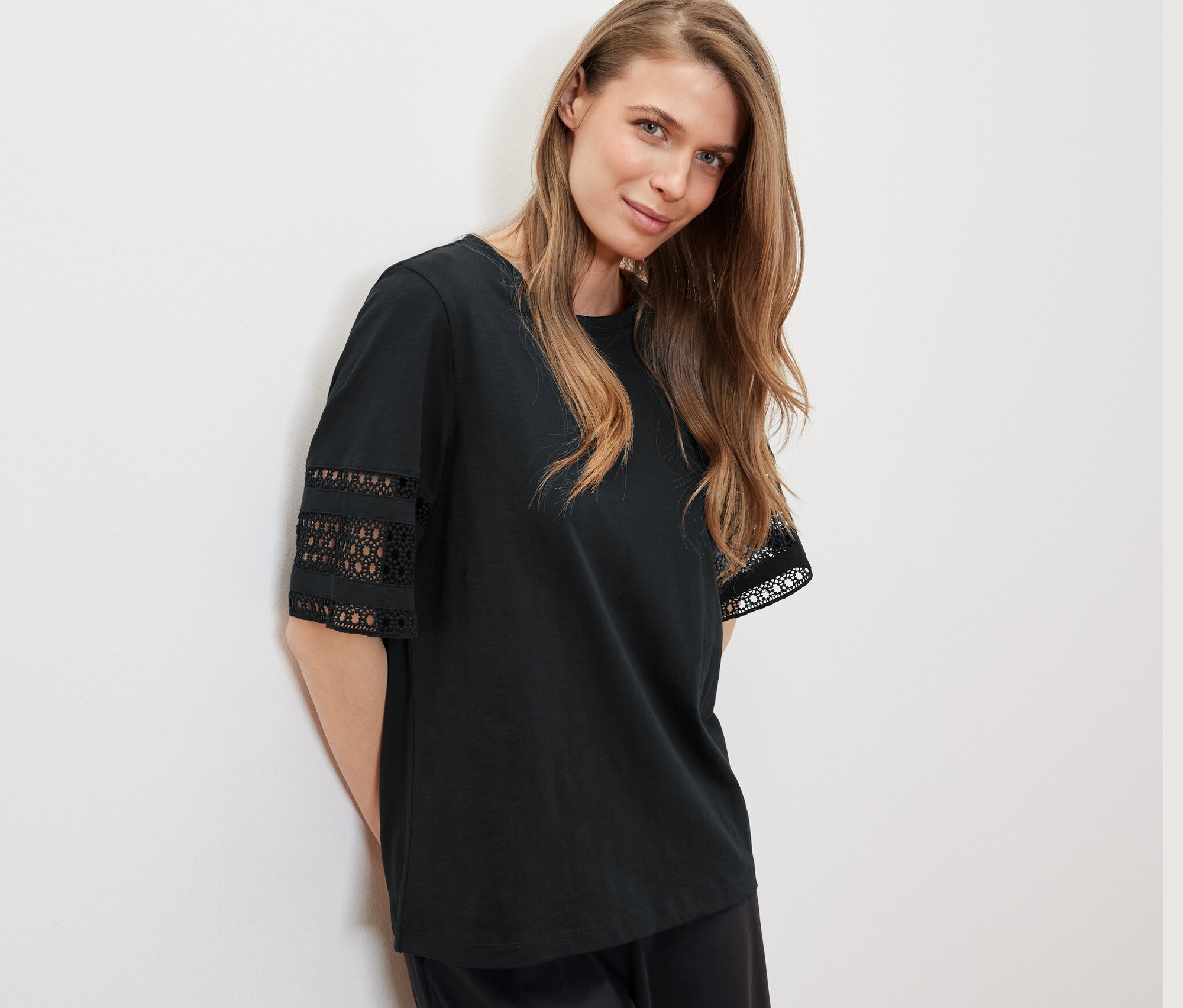 Une femme appuyée contre un mur porte un t-shirt à broderie noir.