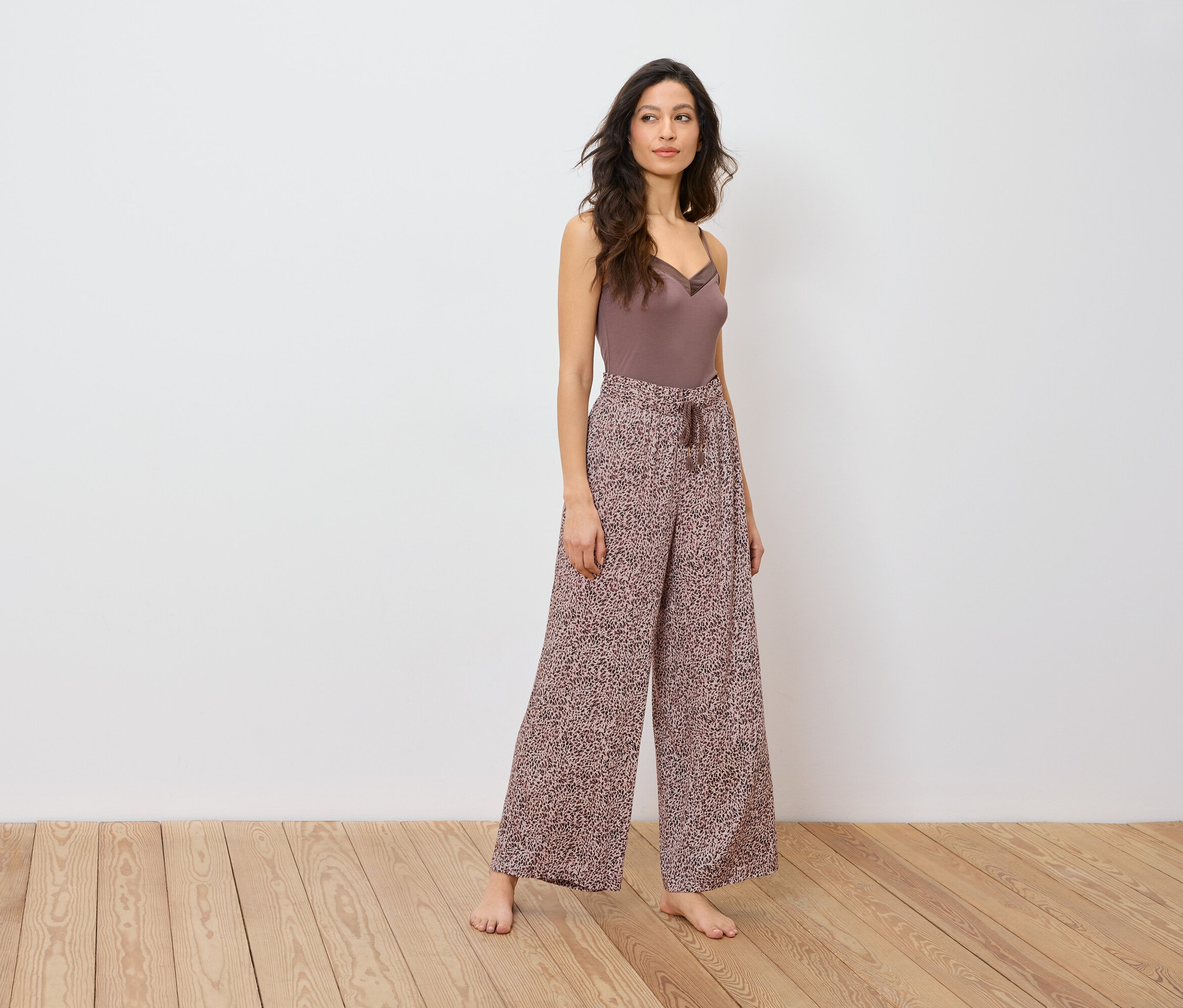 Une femme pose en haut marron et pantalon large à imprimé animalier.