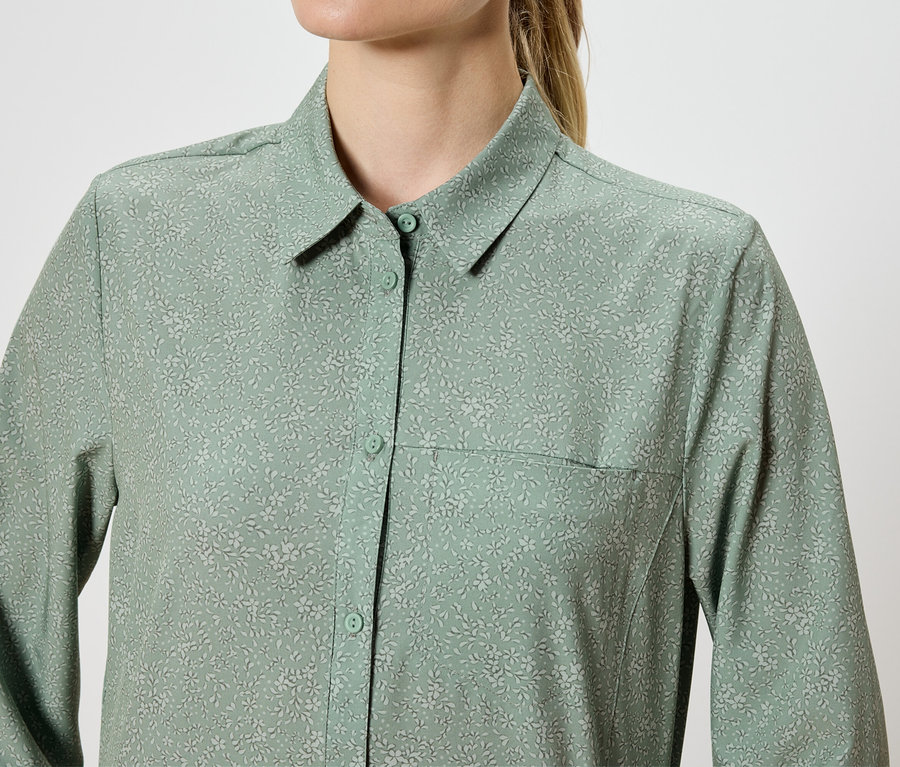 Gros plan d'une femme portant une chemise à manches longues vert clair avec un motif floral.