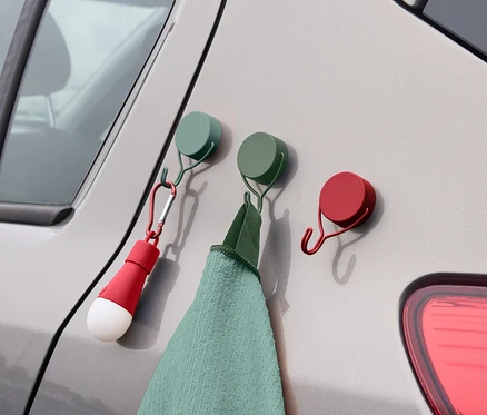 Sur le côté d'une voiture sont accrochés trois crochets colorés auxquels sont suspendus une serviette et une lampe.