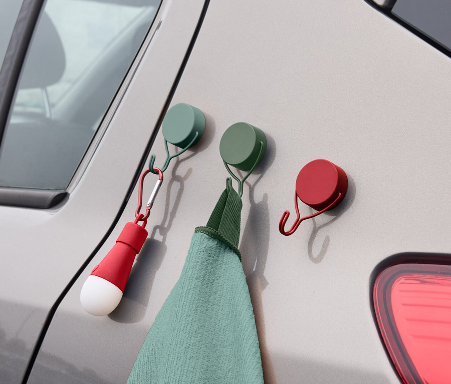 Sur le côté d'une voiture sont accrochés trois crochets colorés auxquels sont suspendus une serviette et une lampe.