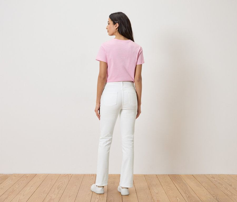 Vue arrière d'une femme aux longs cheveux foncés portant un t-shirt rose, un jean blanc et des chaussures blanches.