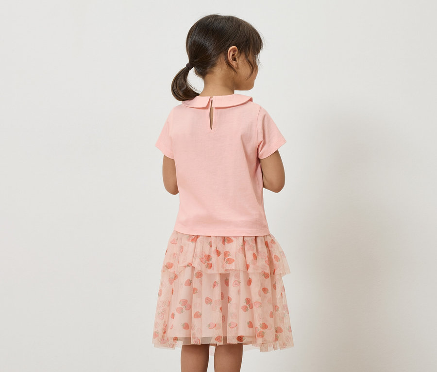 Vue arrière d'une petite fille avec une queue de cheval, portant un t-shirt rose et une jupe en tulle rose avec un motif de fraises.