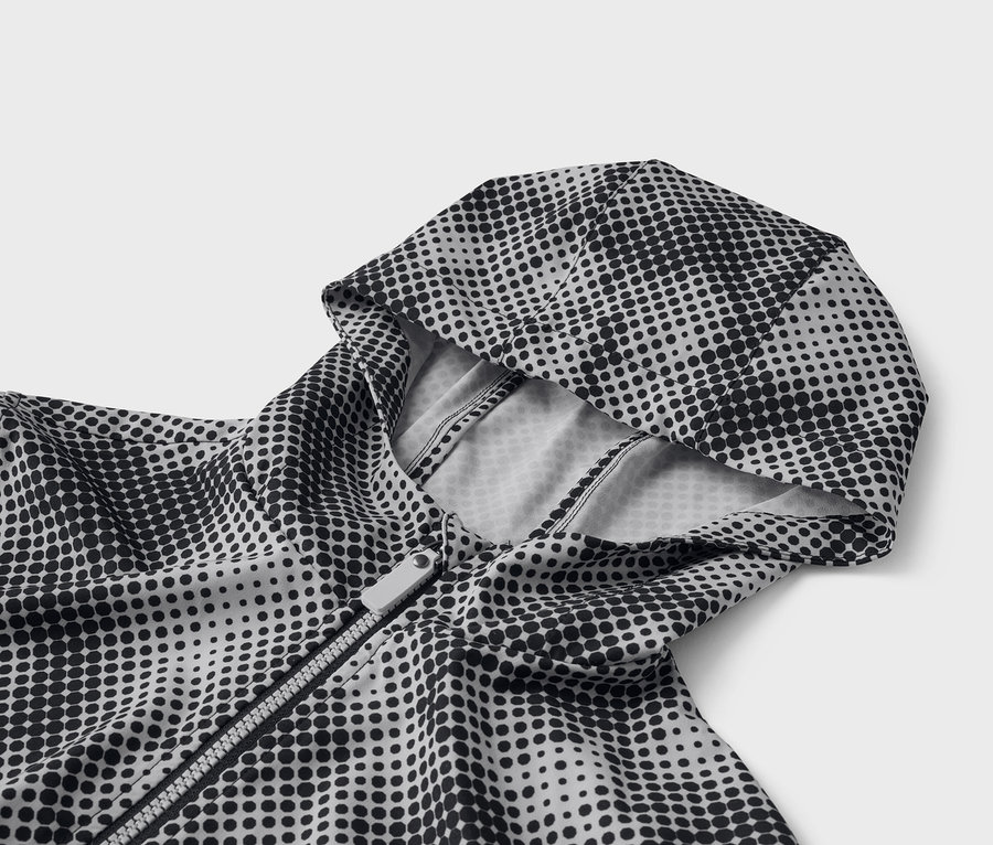 Gros plan d'un blouson à capuche avec un motif à pois noirs et une fermeture éclair argentée.