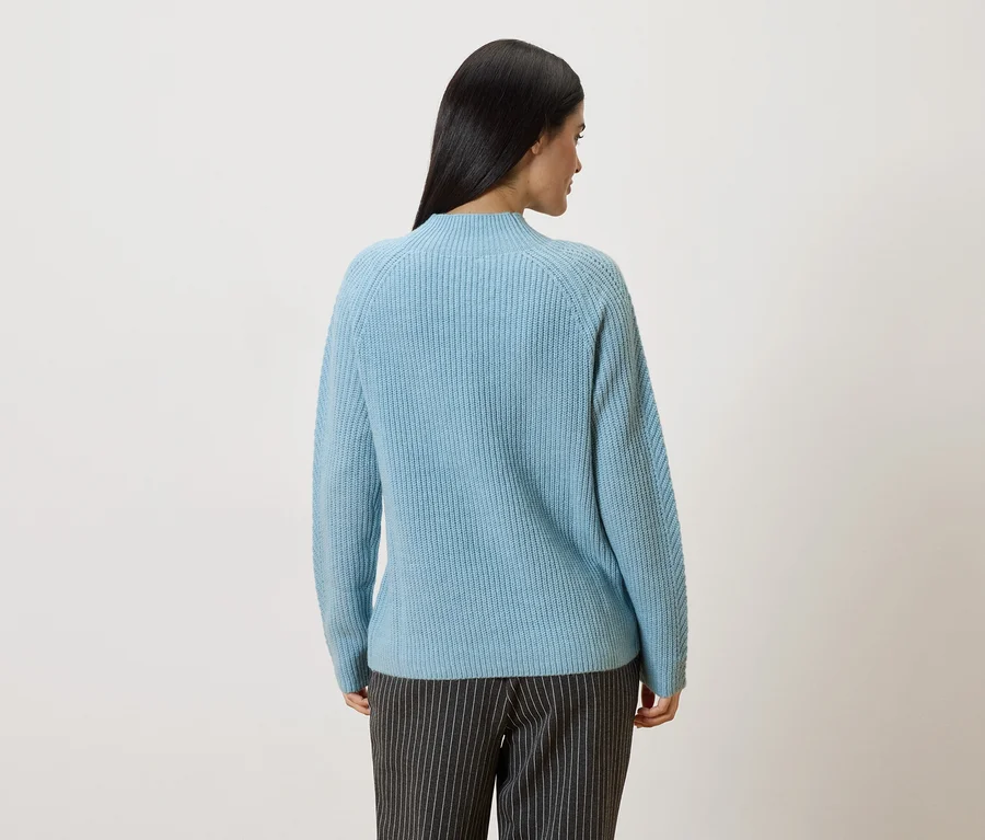 Vue de dos d'une femme aux longs cheveux foncés portant un pull bleu clair et un pantalon gris rayé.