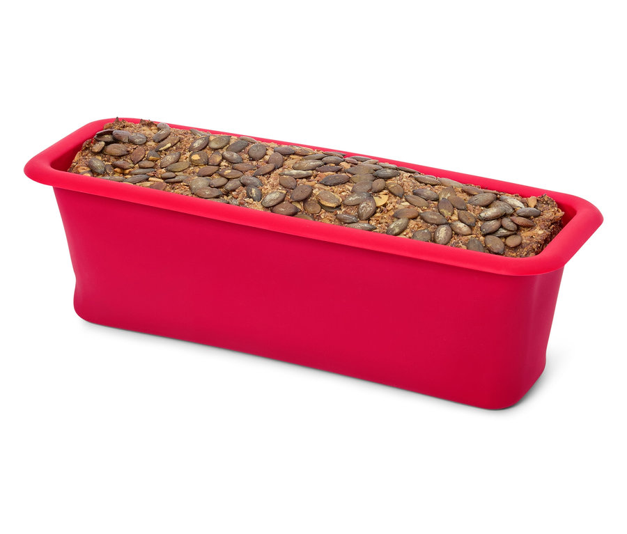 Un moule à pain en silicone rouge rempli de pain garni de graines de citrouille.