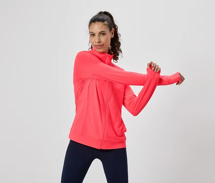 Femme s'étirant dans une veste de survêtement rose et un legging.