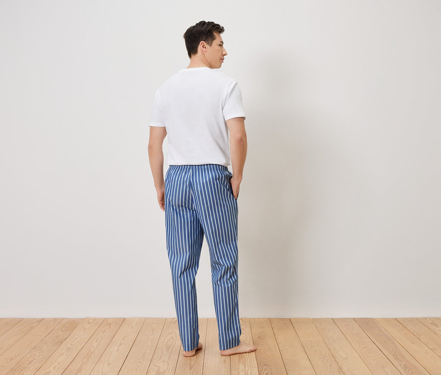 Homme vu de dos portant un pantalon de pyjama rayé bleu et blanc et un t-shirt blanc.