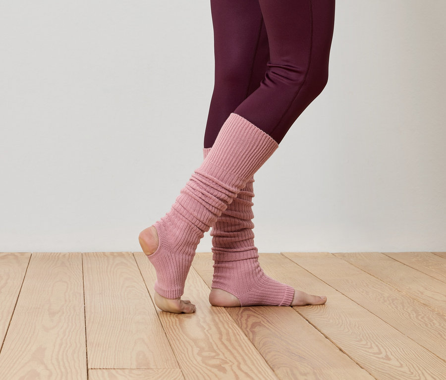 Gros plan d'une personne portant des leggings bordeaux et des guêtres roses côtelées sur un plancher en bois.