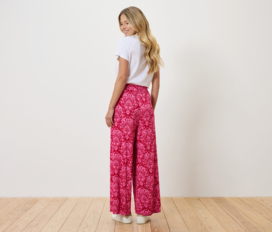 Une femme aux cheveux blonds porte un t-shirt blanc et un pantalon rose large à motifs.