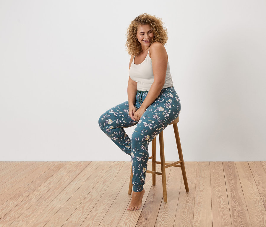 Femme aux cheveux bouclés assise sur un tabouret, portant un débardeur et un legging à fleurs.