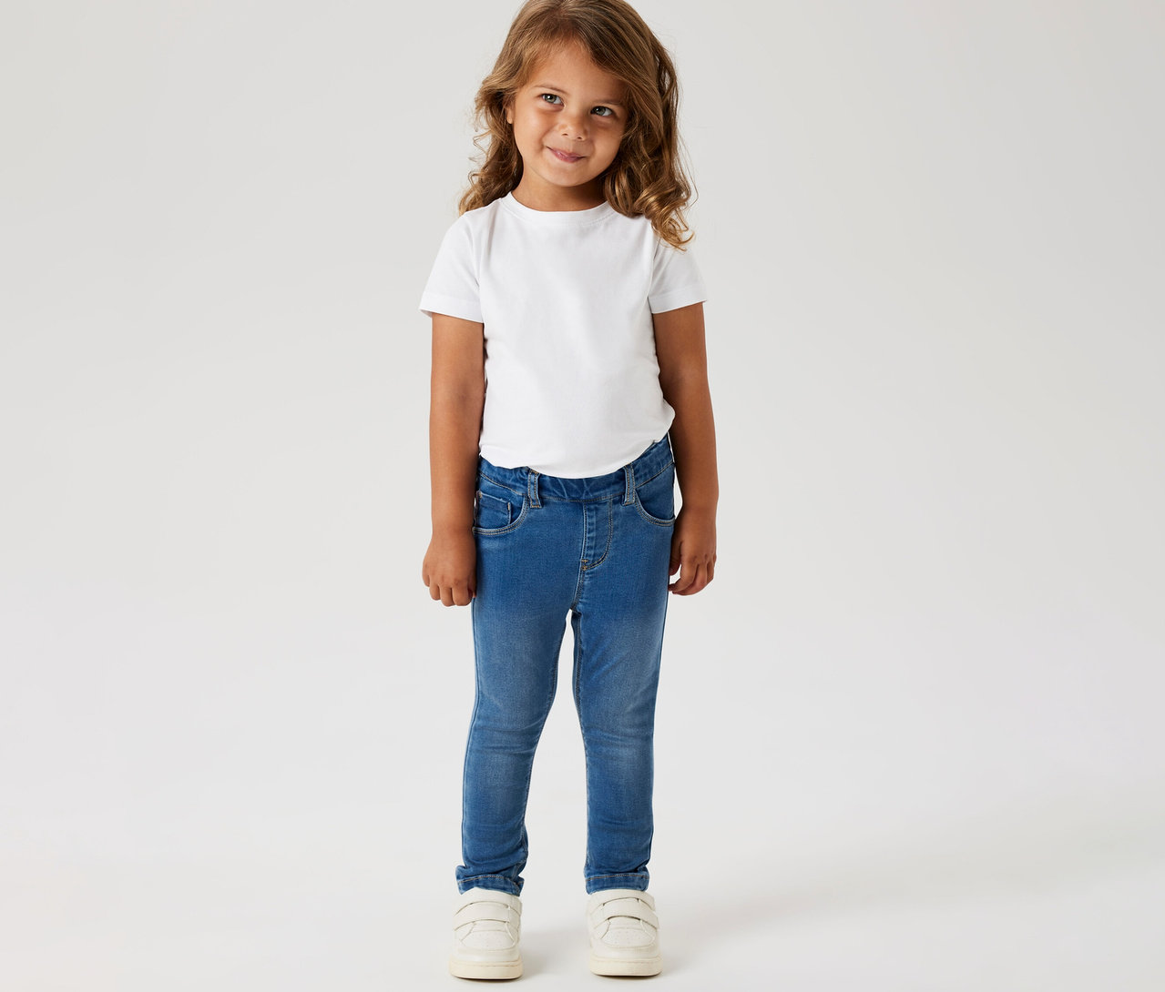 Une fille porte un t-shirt blanc, un jegging pour enfant NAME IT et des chaussures blanches.