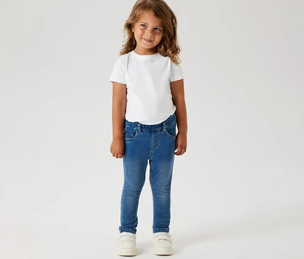 Une fille porte un t-shirt blanc, un jegging pour enfant NAME IT et des chaussures blanches.