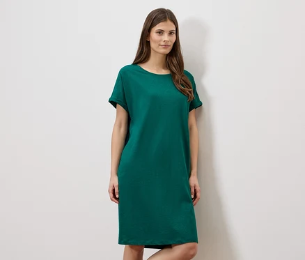 Femme portant une robe verte courte devant un mur blanc.