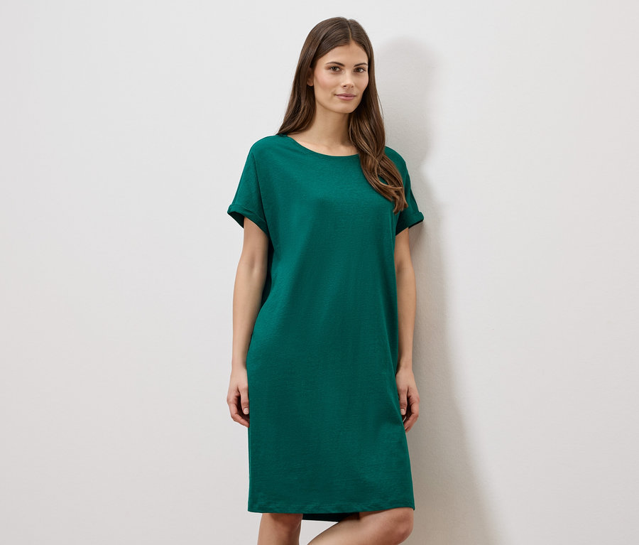 Femme portant une robe verte courte devant un mur blanc.