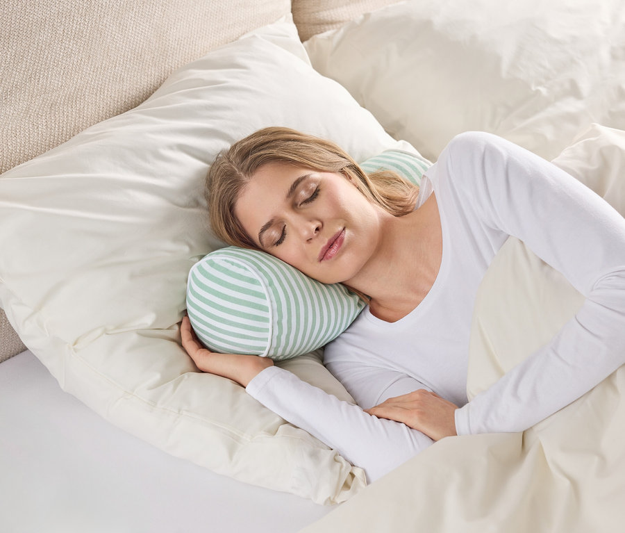 Une femme dort dans un lit avec un oreiller cylindrique rayé sous sa tête.