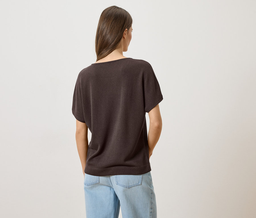 Vue de dos d'une femme aux cheveux bruns portant un t-shirt marron et un jean bleu clair.