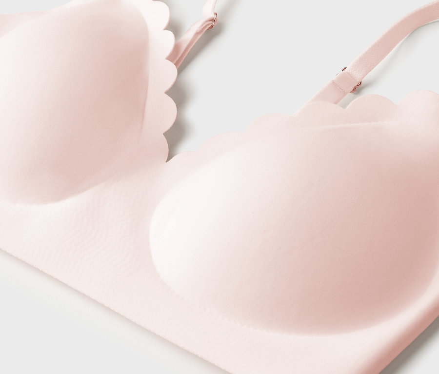 Gros plan d'un soutien-gorge rose pâle avec des bonnets moulés et des bretelles réglables sur fond blanc.