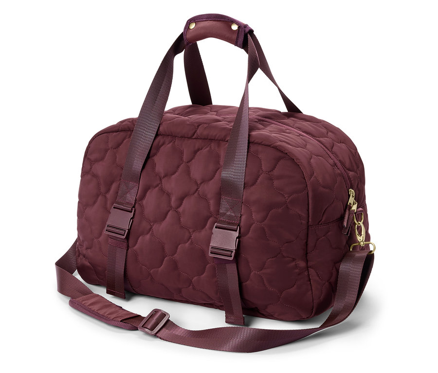 Un sac de voyage bordeaux matelassé avec des poignées et une bandoulière est posé sur un fond blanc.