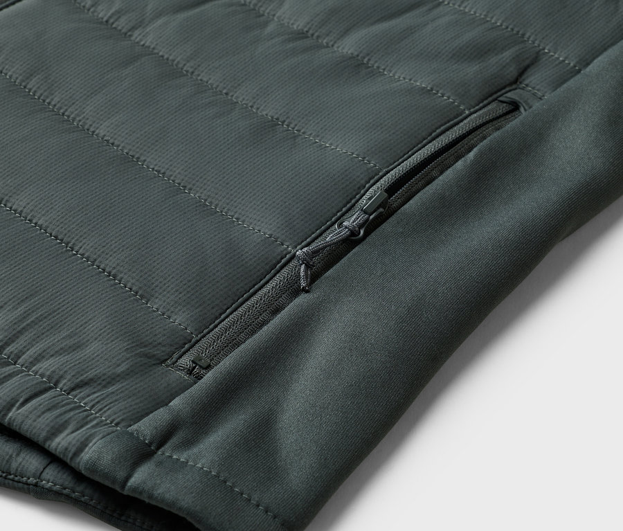 Gros plan d'une veste matelassée vert olive avec une poche zippée sur la manche.