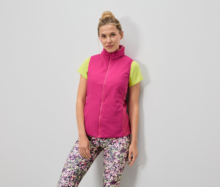 Une femme porte un gilet rose sur un t-shirt vert clair et un legging à fleurs.