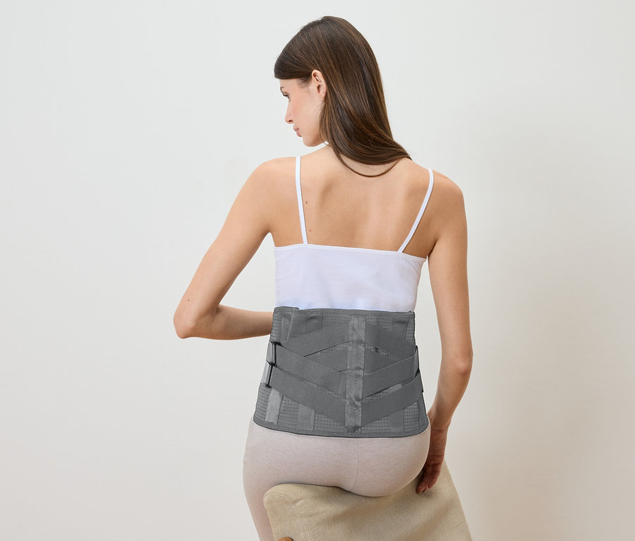Une femme est assise sur une chaise et porte un support lombaire gris.