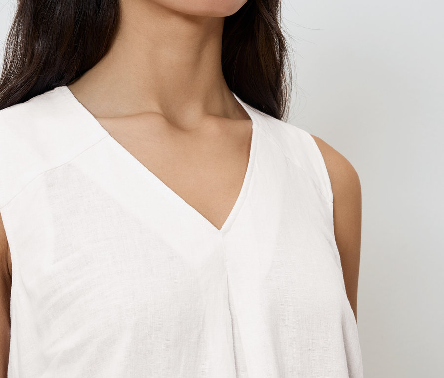 Gros plan d'une femme portant un haut sans manches blanc à col en V.