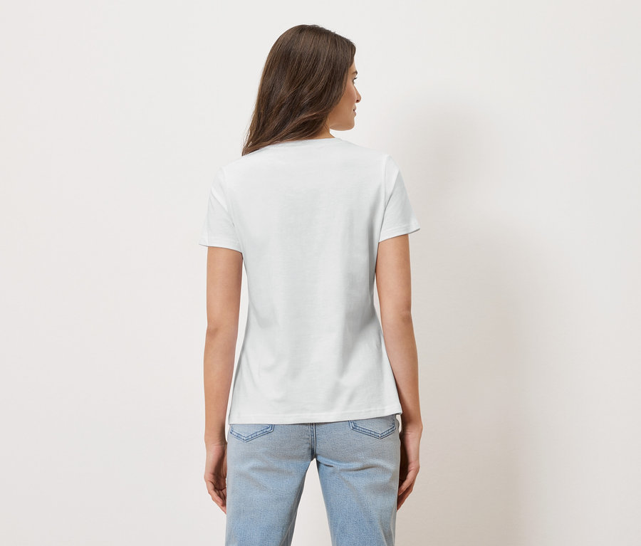 Une femme aux longs cheveux bruns porte un t-shirt blanc et un jean bleu.