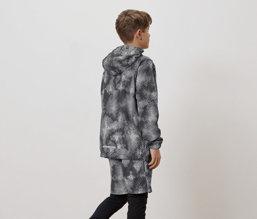 Un garçon vu de dos porte un imperméable à motifs noirs et blancs avec capuche et un short sur un legging noir.